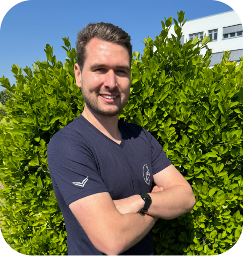 Marino Hoffmann, junger Mann mit kurzem brauen Haar, freundliches Lächeln, blaues ST-Shirt mit logo der Praxis und verschränkten Armen