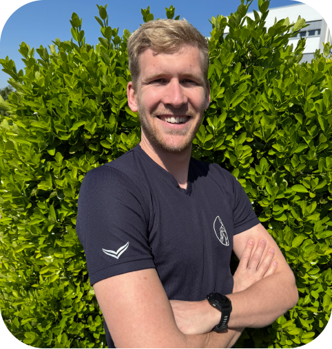 Marvin Thyssen, blonder junger Mann mit kurzem Bart, freundlcihes Lächeln, blaues ST-Shirt mit logo der Praxis und verschränkten Armen